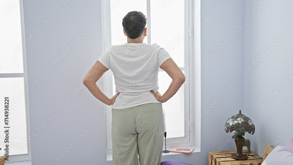 A man in casual attire standing in a bright bedroom with hands on hips, adjacent to a yoga mat and lamp, portraying a relaxed domestic environment. A man in casual attire standing in a bright bedroom with hands on hips, adjacent to a yoga mat and lamp, portraying a relaxed domestic environment.