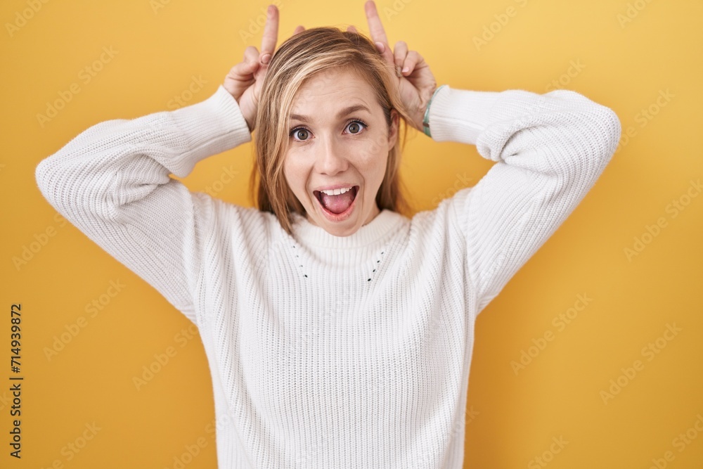 Young caucasian woman wearing white sweater over yellow background posing funny and crazy with fingers on head as bunny ears, smiling cheerful Young caucasian woman wearing white sweater over yellow background posing funny and crazy with fingers on head as bunny ears, smiling cheerful