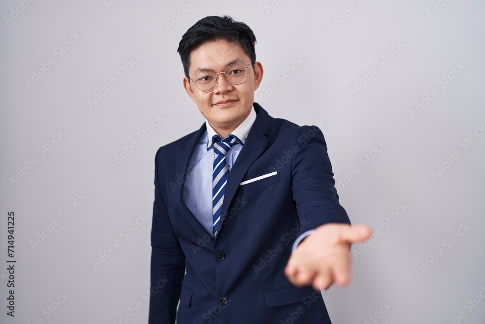 Young asian man wearing business suit and tie smiling cheerful offering palm hand giving assistance and acceptance. Young asian man wearing business suit and tie smiling cheerful offering palm hand giving assistance and acceptance.