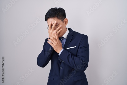 Young asian man wearing business suit and tie with sad expression covering face with hands while crying. depression concept.