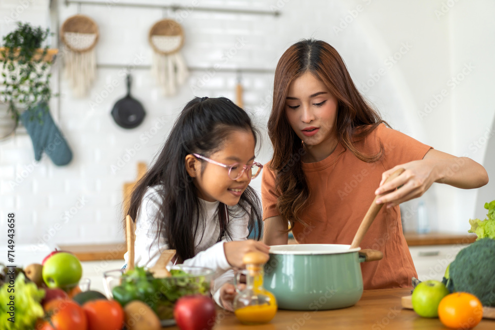 Portrait of happy love asian family mother with little asian girl daughter child help cooking food healthy eat with fresh vegetable testing smell soup in a pot with spoon.help mom in kitchen at home