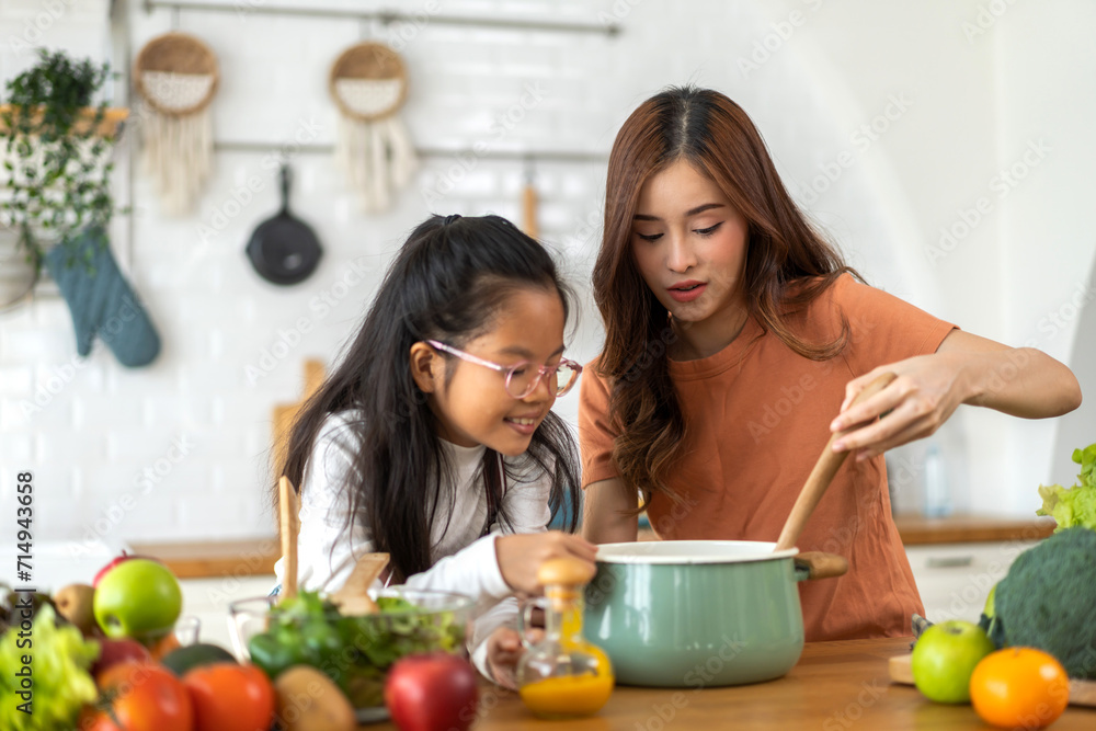 Portrait of happy love asian family mother with little asian girl daughter child help cooking food healthy eat with fresh vegetable testing smell soup in a pot with spoon.help mom in kitchen at home Portrait of happy love asian family mother with little asian girl daughter child help cooking food healthy eat with fresh vegetable testing smell soup in a pot with spoon.help mom in kitchen at home