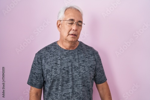 Middle age man with grey hair standing over pink background looking sleepy and tired, exhausted for fatigue and hangover, lazy eyes in the morning. © Krakenimages.com