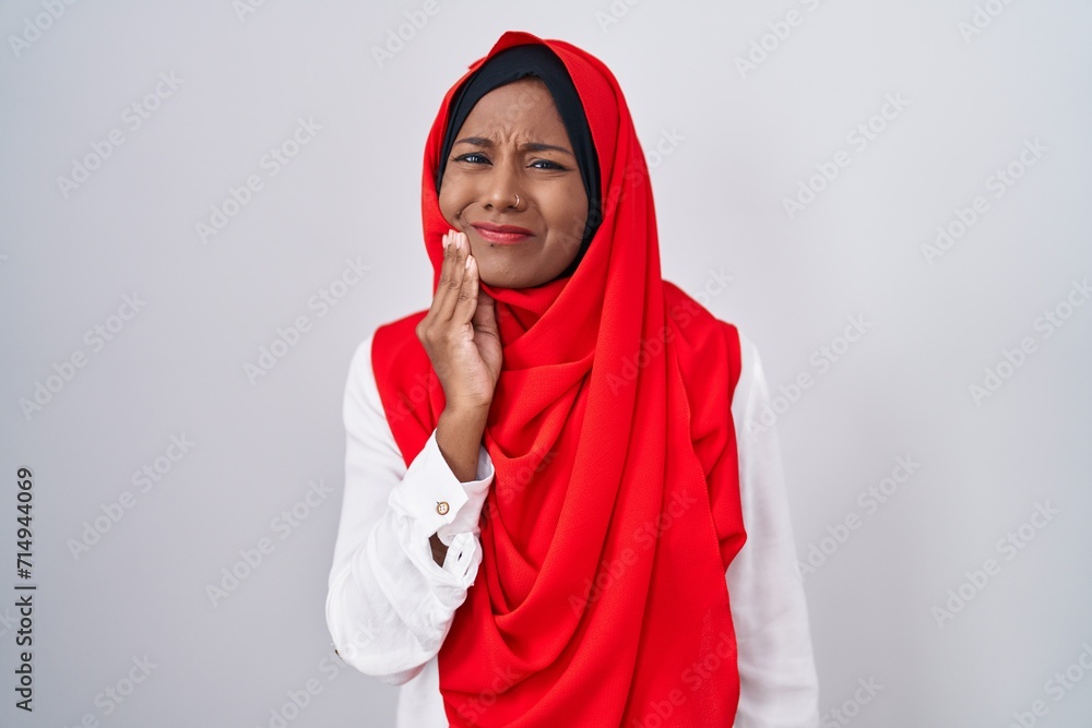 Young arab woman wearing traditional islamic hijab scarf touching mouth with hand with painful expression because of toothache or dental illness on teeth. dentist Young arab woman wearing traditional islamic hijab scarf touching mouth with hand with painful expression because of toothache or dental illness on teeth. dentist