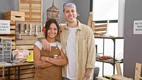 A smiling man and woman, both in casual wear, embracing in a well-organized carpentry workshop, reflecting teamwork and partnership. photo