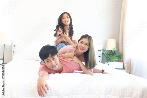 Happy Asian family having fun in bedroom. Father, mother and daughter playing together during lying on white bed. Parents having good memory with kid child girl at home. parenthood and childhood