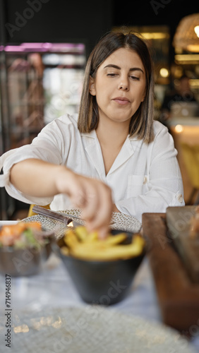 Young beautiful hispanic woman eating french fries at the restaurant