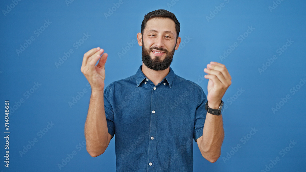Fototapeta premium Young hispanic man smiling confident doing money gesture over isolated blue background