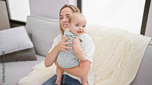 At home, a joyful mother sitting on the sofa, hugging and laughing with her baby daughter, radiating happiness and confidence, enjoying their casual time indoors in the living room.