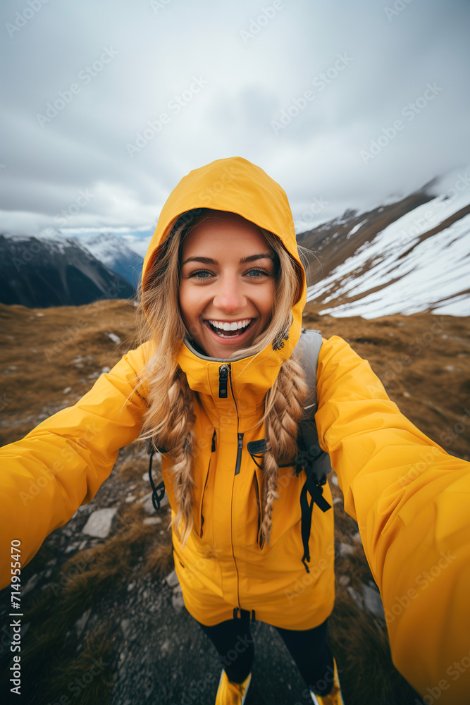A woman takes a selfie of herself in a yellow jacket on a mountain trip in the nature. 