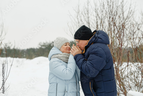 An elderly caring man warms his wife's hands with his breath on the street.