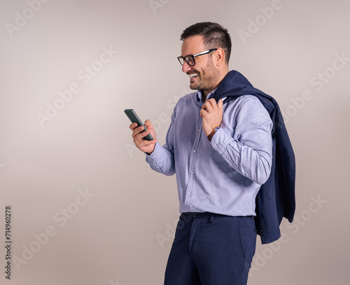 Smiling handsome manager with blazer using smartphone for social media marketing on white background © Moon Safari
