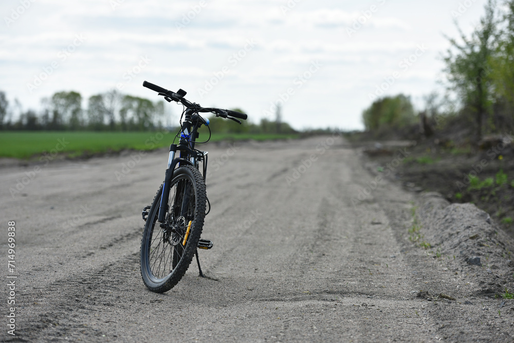 Obraz premium Mountain bike. stands on a field road. spring or autumn. concept of cycling, repair or breakage, sports, outdoor activities. bike on trail, front wheel in focus. healthy lifestyle