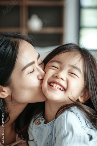 Close up of beautiful daughter kissing mother on cheek at home Asian little girl giving kiss