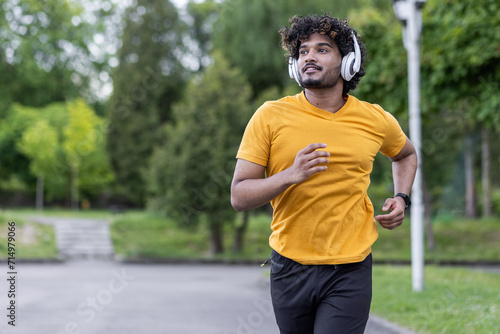 Indian young man doing sports and training in the morning, wearing headphones running in the park