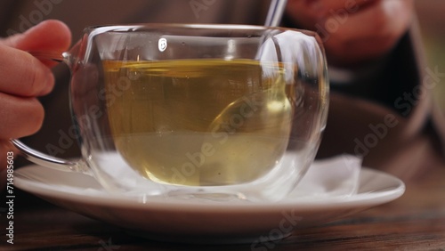 Lady stirs green tea with spoon in transparent glass cup on wooden table in park cafe. Lady takes tea break rotating spoon to mix sugar. Tea for maintaining lady figure stirring hot drink with spoon