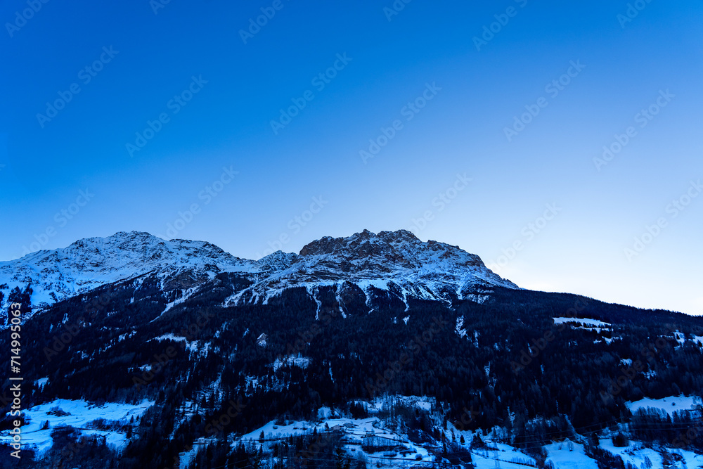 Early dawn landscape of the snow-covered Swiss Alps under a blue sky, all enveloped in a fairytale blue light