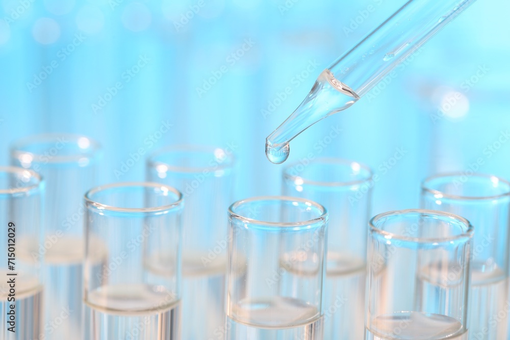 Laboratory analysis. Dripping liquid from pipette into glass test tube on light blue background, closeup Laboratory analysis. Dripping liquid from pipette into glass test tube on light blue background, closeup
