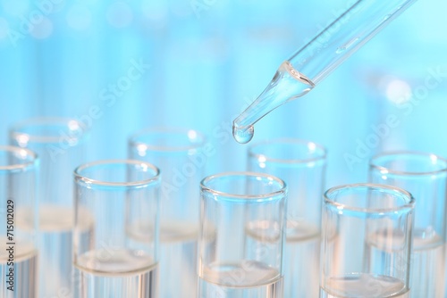 Laboratory analysis. Dripping liquid from pipette into glass test tube on light blue background, closeup