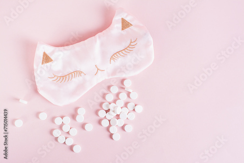 Sleeping pills and sleep mask on pink background top view