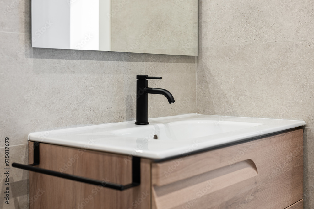 Fototapeta premium Close-up of a sink with a black tap and a mirror on the background of a gray stone wall. Concept new and stylish plumbing in new residential complexes ready for delivery