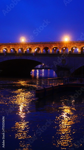 Reflexion de lumière sur la Seine, la nuit, ciel bleu foncé, surface eau, en plein centre ville, circulation de péniche, éclairage de lampadaires, façade de bâtiment ou pont ancien, photographique