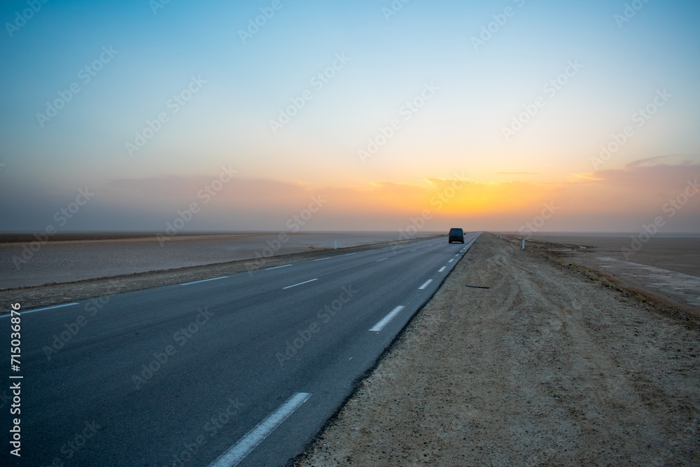 Beautiful colourful sunset over endless empty road in middle of desert. Asphalt highway in Tunisia, North Africa.