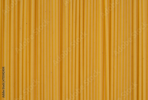 Parallel lines of uncooked spaghetti create a linear pattern on a yellow background, perfect for culinary and food themes.