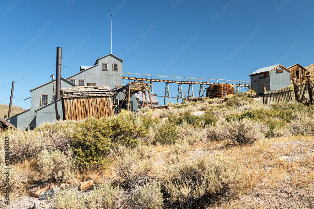 Abandoned Brodie Ghost Twon mining operation buildings deserted in the arid desert landscape of California with sagebrush and a clear cloudless blue sky.
