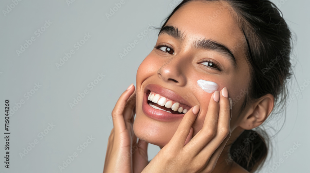 Close-up of a woman with clear blue eyes and flawless skin applying a white cream on her cheek with her fingers, exemplifying a skincare routine. Close-up of a woman with clear blue eyes and flawless skin applying a white cream on her cheek with her fingers, exemplifying a skincare routine.