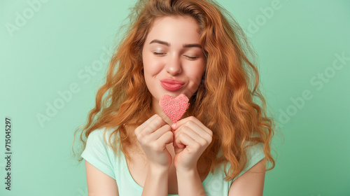 Close-up portrait of attractive lovely coquettish cheerful cheery wavy-haired girl holding in hands small little heart sending you kiss isolated over pastel green background. photo