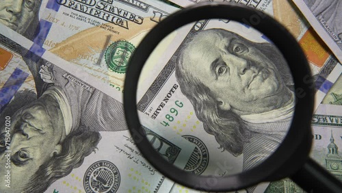 United States one hundred dollar bills and a black magnifying glass. Economy, finance and inflation. Hand with magnifying glass on a background of dollar bills. The note under a magnifying glass photo