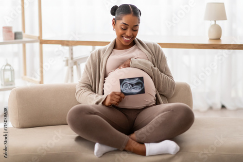 Happy black pregnant woman sitting on couch with baby sonography photo