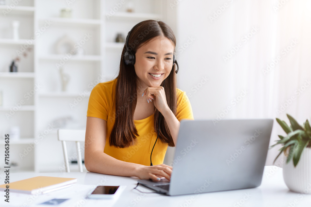 Focused asian woman wearing headset working on her laptop in home office Focused asian woman wearing headset working on her laptop in home office