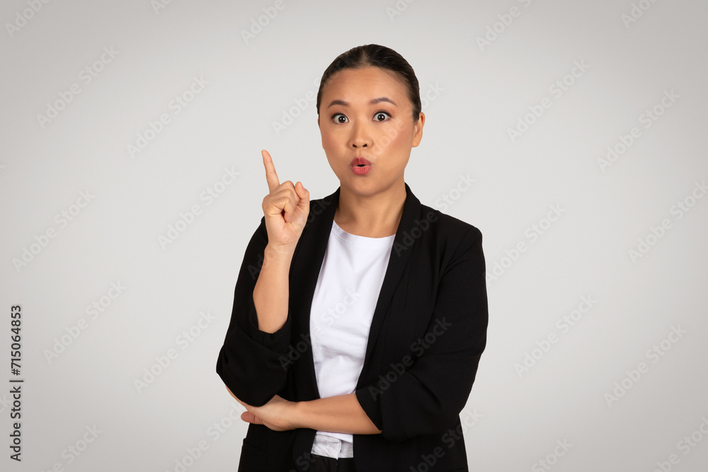 Surprised Asian businesswoman in a black blazer pointing upwards, having an idea Surprised Asian businesswoman in a black blazer pointing upwards, having an idea