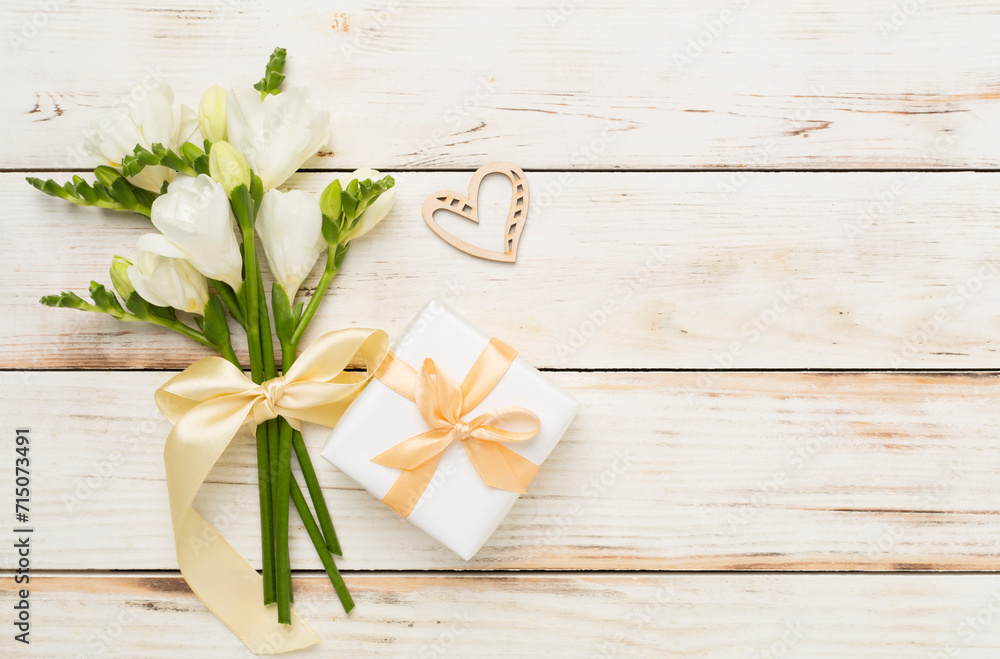 Gift box with freesia flower on wooden background, top view Gift box with freesia flower on wooden background, top view