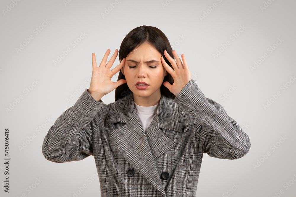 Stressed woman in checkered coat with headache, holding temples Stressed woman in checkered coat with headache, holding temples