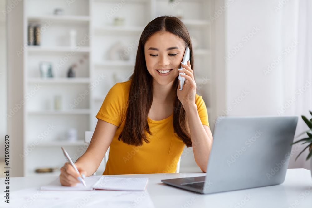 Home Office. Young Asian Woman Talking On Cellphone And Taking Notes Home Office. Young Asian Woman Talking On Cellphone And Taking Notes