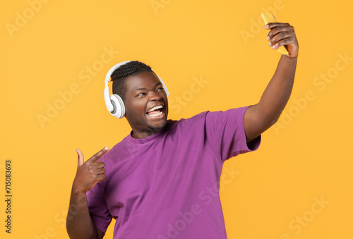 Cheerful african man making selfie on smartphone wearing headphones, studio