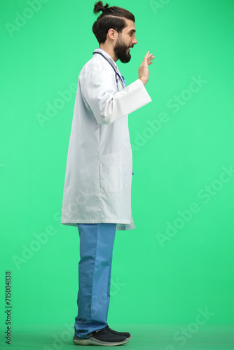 A male doctor, full-length, on a green background, waving his hand