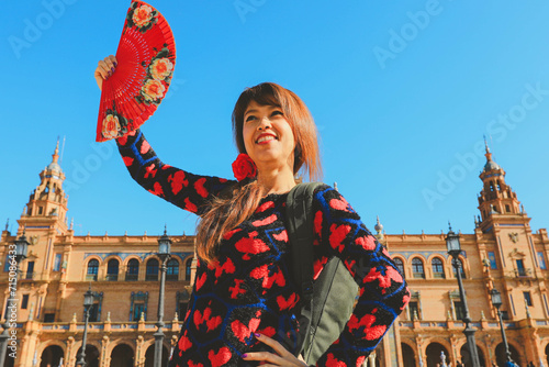 Beautiful asian woman holding Spanish  fan in front of Plaza de Espana in Seville, Spain during her vacation