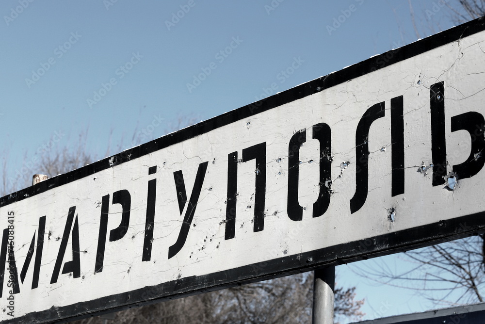 War in Ukraine. A road sign with inscription in Ukrainian - Mariupol, pierced by bullets during war in Ukraine. Donetsk