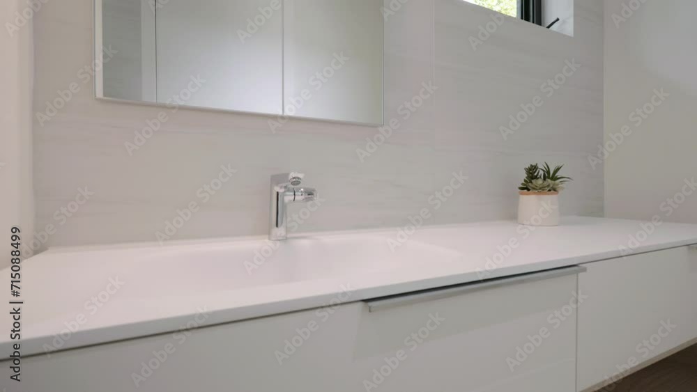 Modern and minimalist bathroom sink on sleek white countertop. Small potted plant adding greenery to space and the mirror above fauset enhancing room brightness Modern and minimalist bathroom sink on sleek white countertop. Small potted plant adding greenery to space and the mirror above fauset enhancing room brightness