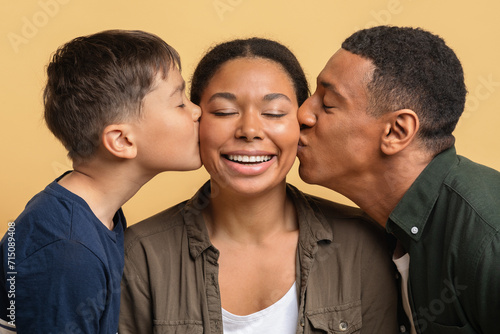 Loving black father and son kissing happy young woman