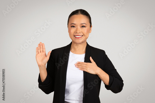 Professional Asian businesswoman making a pledge or oath gesture with a raised right hand photo