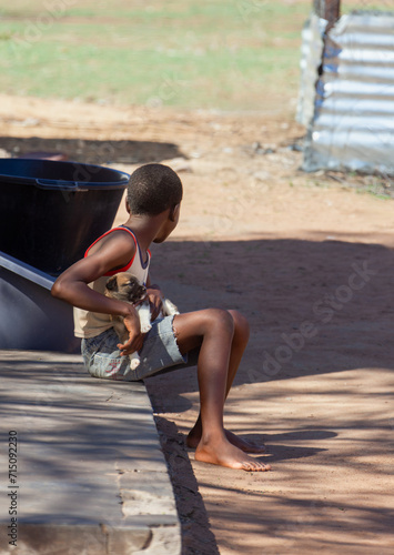Fototapeta Naklejka Na Ścianę i Meble -  african child holding a puppy resting in the yard sitting in the shade