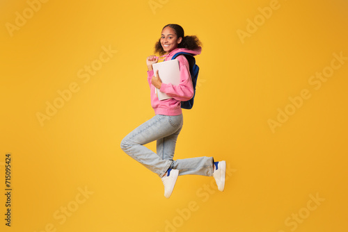 Smiling african american youngster girl jumping with her backpack, studio