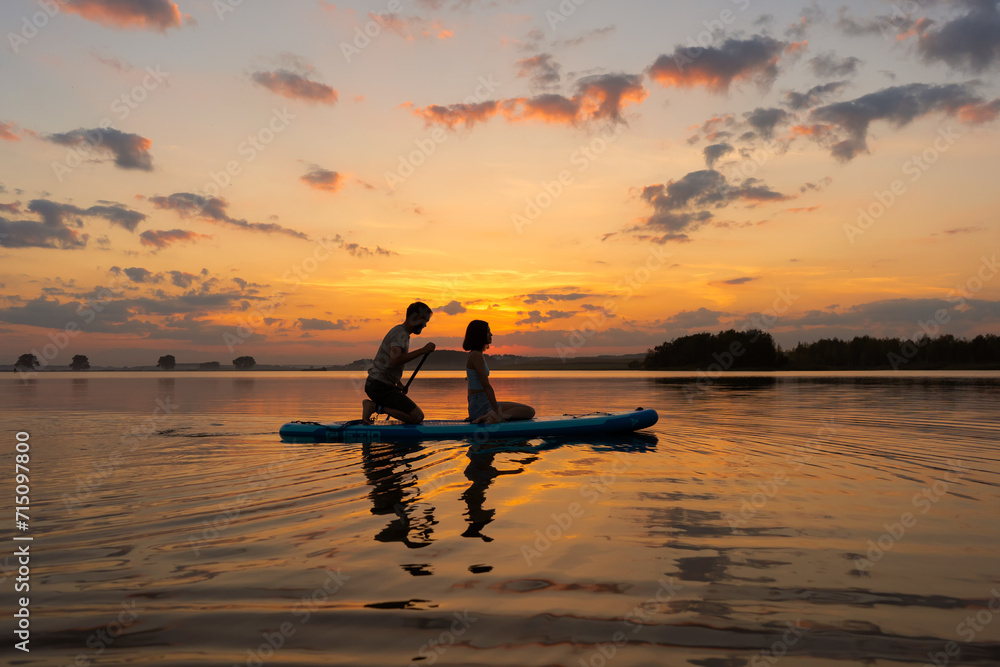 silhouette of couple paddleboarding at lake during sunset together. Concept of active family tourism and supping. Family enjoy vacation