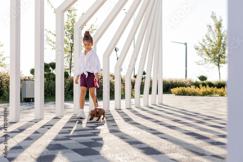 beautiful little girl with long hair walks with a dachshund dog in the summer in the city park