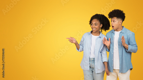 A young woman and man in casual attire are excitedly pointing to something off-camera
